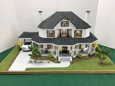 a model house is displayed on a green mat in front of a white building with black roof