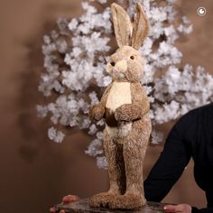 a person holding a stuffed rabbit in front of a fake tree