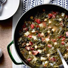 a pot filled with stew and vegetables on top of a wooden table next to silverware