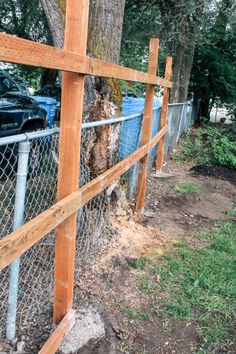 a wooden fence next to a tree and some cars parked in the back yard behind it