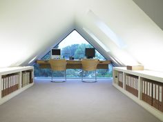 an attic office with two desks and computer monitors on top of the desk, in front of a large window