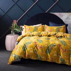 a bed with yellow comforter and pillows in a room next to a plant on a table