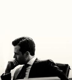 a black and white photo of a man in a suit sitting at a desk with his hand on his chin