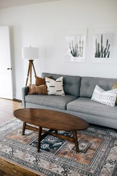 a living room with a gray couch and wooden coffee table in front of two pictures on the wall