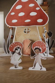 two paper dolls are standing in front of a mushroom house