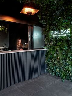 the outside of a restaurant with plants growing on the wall and an illuminated sign that reads fuel bar