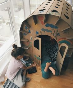 two children playing in a cardboard play house