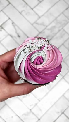 a hand holding a cupcake with pink and white frosting