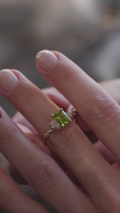 a woman's hand holding an engagement ring with a green gemstone in it