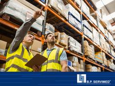 two men in yellow vests standing next to each other with boxes on the shelves behind them