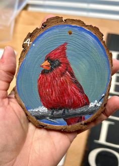 a hand holding a piece of wood with a red bird painted on it's face