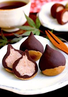 three pieces of chocolate covered pastries on a white plate next to a cup of tea