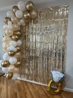 balloons and streamers are hanging in front of a backdrop made of gold, white and silver confetti