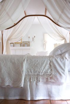 a bed with white sheets and curtains on top of wooden flooring in a bedroom