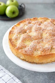 a cake sitting on top of a white plate covered in powdered sugar next to green apples