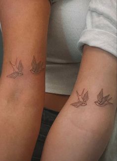 two women with matching tattoos on their arms, one has a bird and the other has a dove