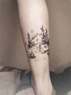 a person's foot with a tent and trees tattoo on the left side of their leg