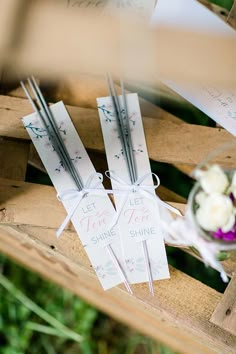 some paper tags with writing on them are sitting on a wooden crate next to flowers