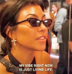 a woman wearing sunglasses is talking to someone on the bus with an ad in front of her that says, my vibe right now is just living life