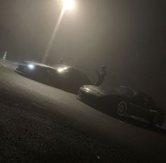 two cars parked on the side of a road at night with street lights in the background