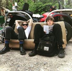 two young men sitting on a couch in the middle of a dirt road with motorcycles behind them