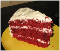 a slice of red velvet cake with white frosting on a yellow plate in front of a black counter