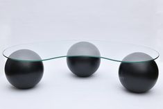 three black balls sitting on top of a glass table next to an oval glass coffee table