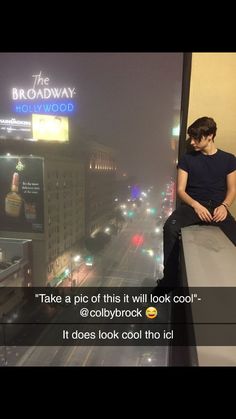 a man sitting on top of a window sill looking out at the street below