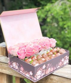 a box filled with pink roses sitting on top of a wooden fence