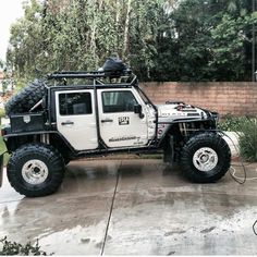 an off road vehicle parked in front of a brick wall with trees and bushes behind it