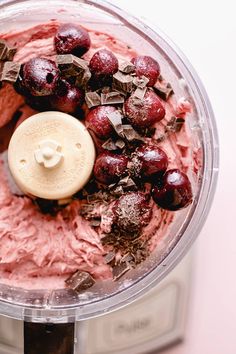 a food processor filled with pink frosting and cherries next to chocolate chips on the side