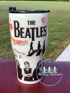 a coffee cup with the beatles on it sitting on a table in front of some grass