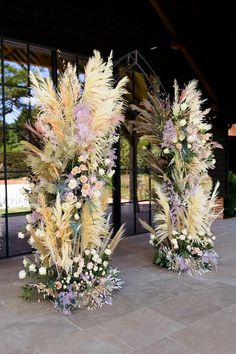 two tall vases filled with flowers sitting on top of a stone floor