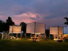 three large screens are set up in the grass at night with lights shining on them