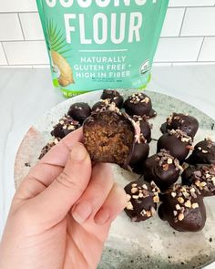 a hand is picking up some chocolates from a plate on the counter next to a bag of coconut flour