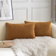 two orange pillows on a white couch in a living room with a framed photograph above them