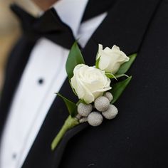 a man in a tuxedo with white flowers and berries on his lapel