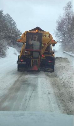 a snow plow driving down a snowy road in the middle of winter with trees on both sides