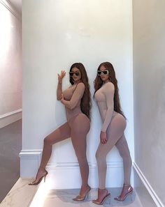 two women in bodysuits standing next to each other with sunglasses on their heads