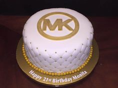 a birthday cake with the letter m in gold and white frosting on a wooden table