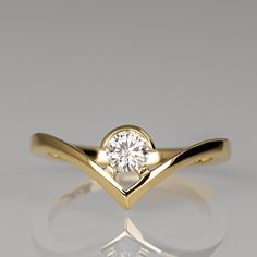 a yellow gold ring with a single diamond in the center, on a reflective surface