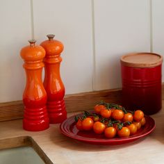 some tomatoes are on a red plate next to pepper shakers and a canister