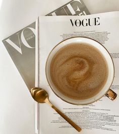 a cup of coffee sitting on top of a table next to a magazine and spoon