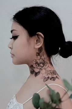 a woman with a flower tattoo on her neck and behind her head is a plant