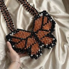 a hand holding a beaded necklace with an orange butterfly on it