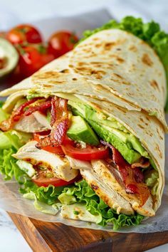 a chicken and lettuce wrap on a cutting board with tomatoes, cucumber and avocado