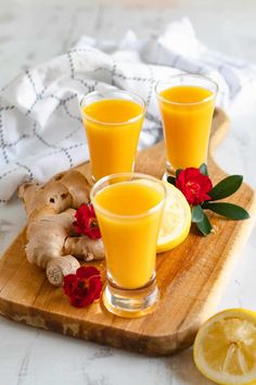 three glasses of orange juice on a cutting board with sliced lemons and fresh ginger