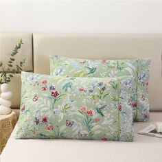 two pillows sitting on top of a bed next to a vase with flowers in it