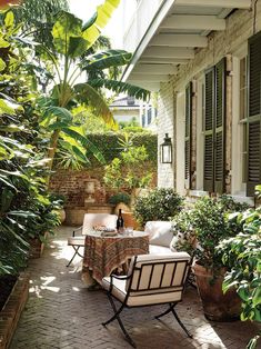 an outdoor patio with chairs, table and potted plants on the side of it