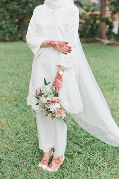 a woman in white is wearing a veil and holding a bouquet with flowers on it